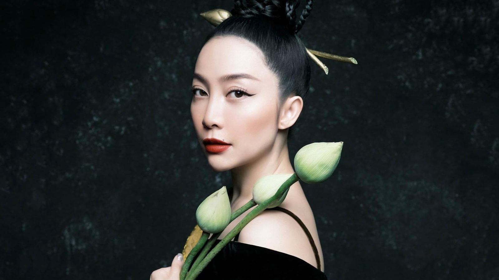A portrait of Linh Nga in black velvet holding lotus buds, her hair dressed with gold ornaments.