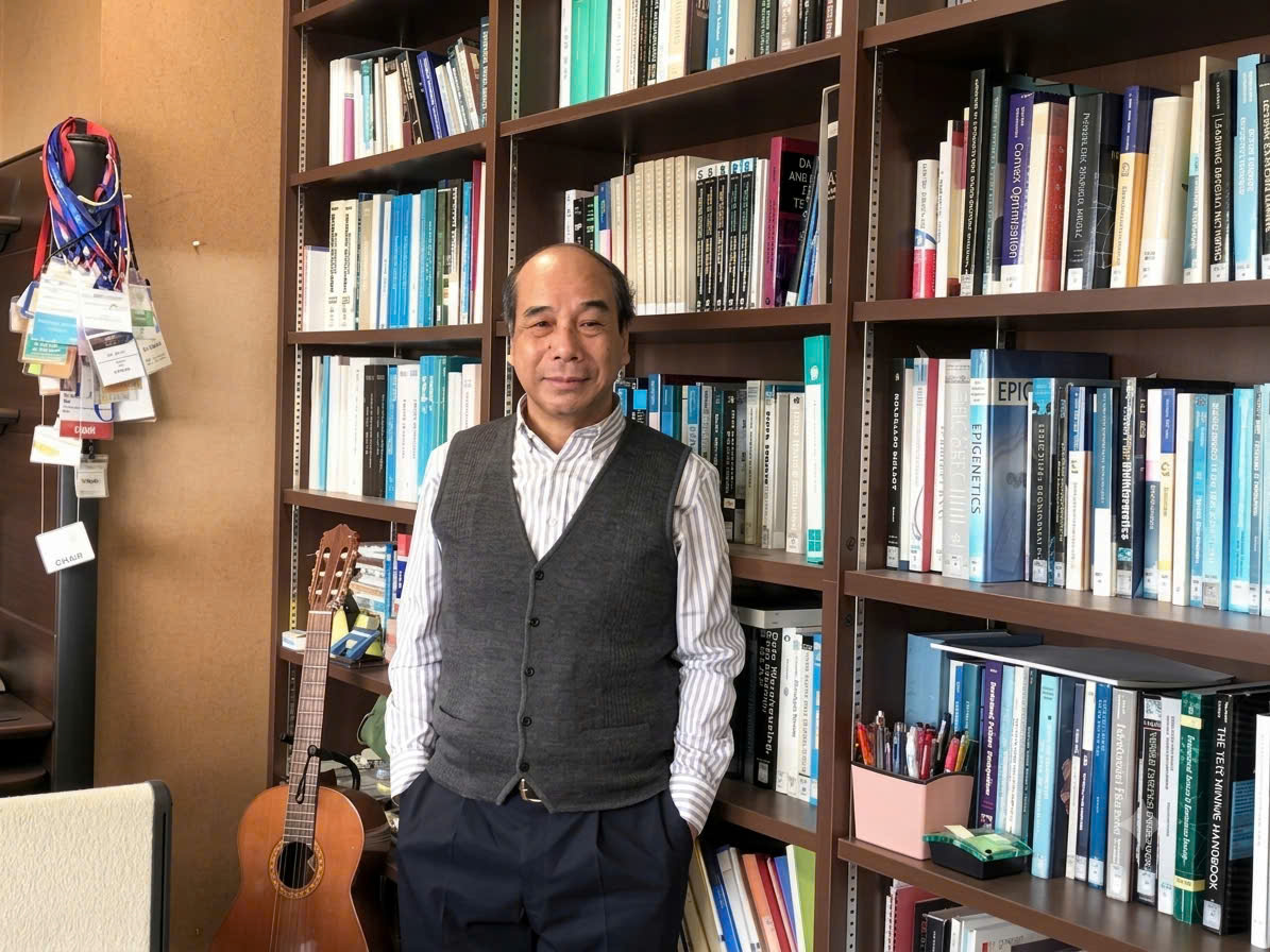 Ho Tu Bao stands in his office in front of a full bookshelf, with a classical guitar beside him