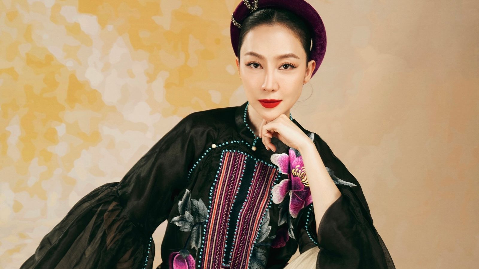 Linh Nga in a black embroidered ao dai and a deep purple velvet headpiece against a gold-flecked backdrop