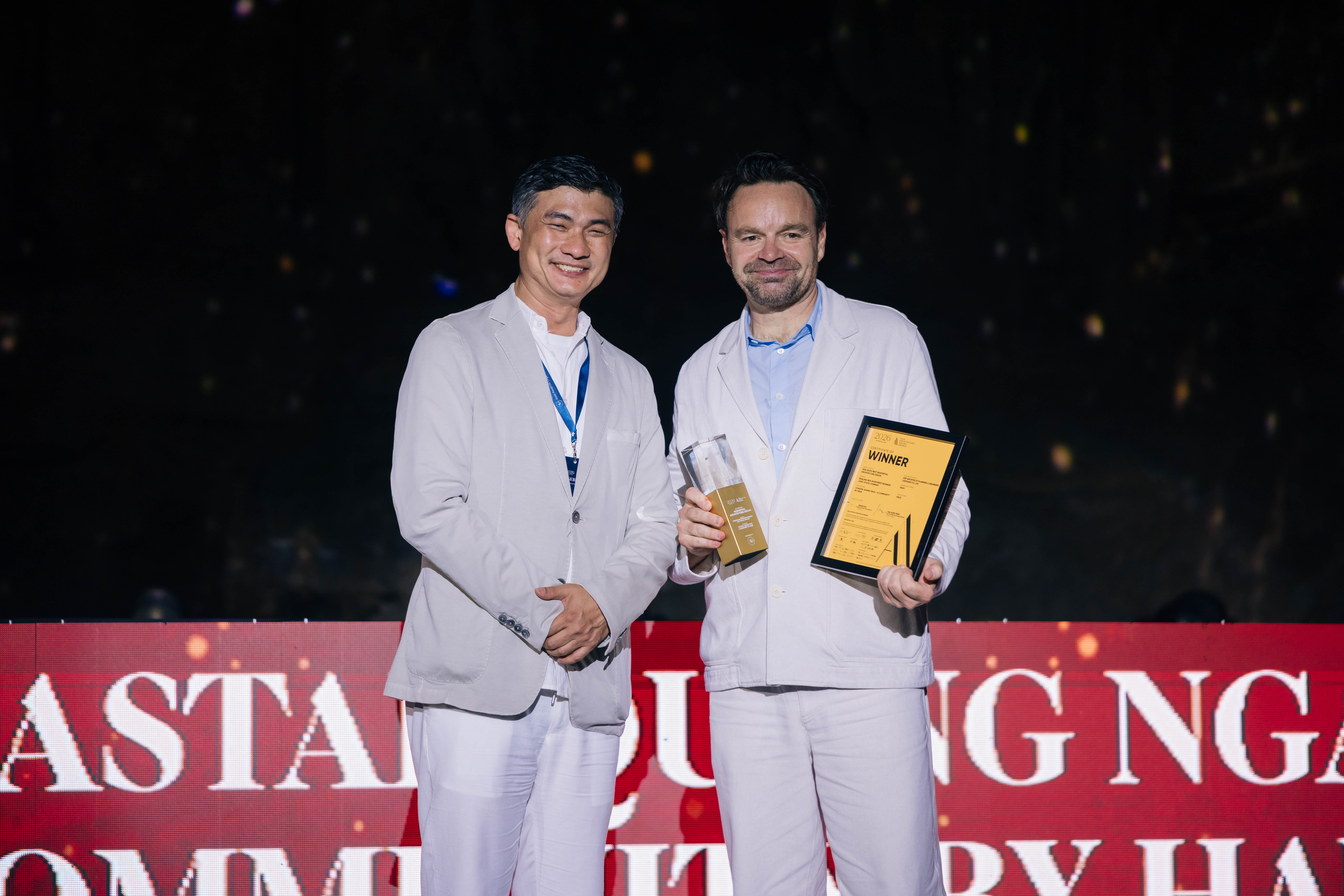 Two men holding a trophy and a WINNER certificate on stage at the 2026 Asia Architecture Design Awards