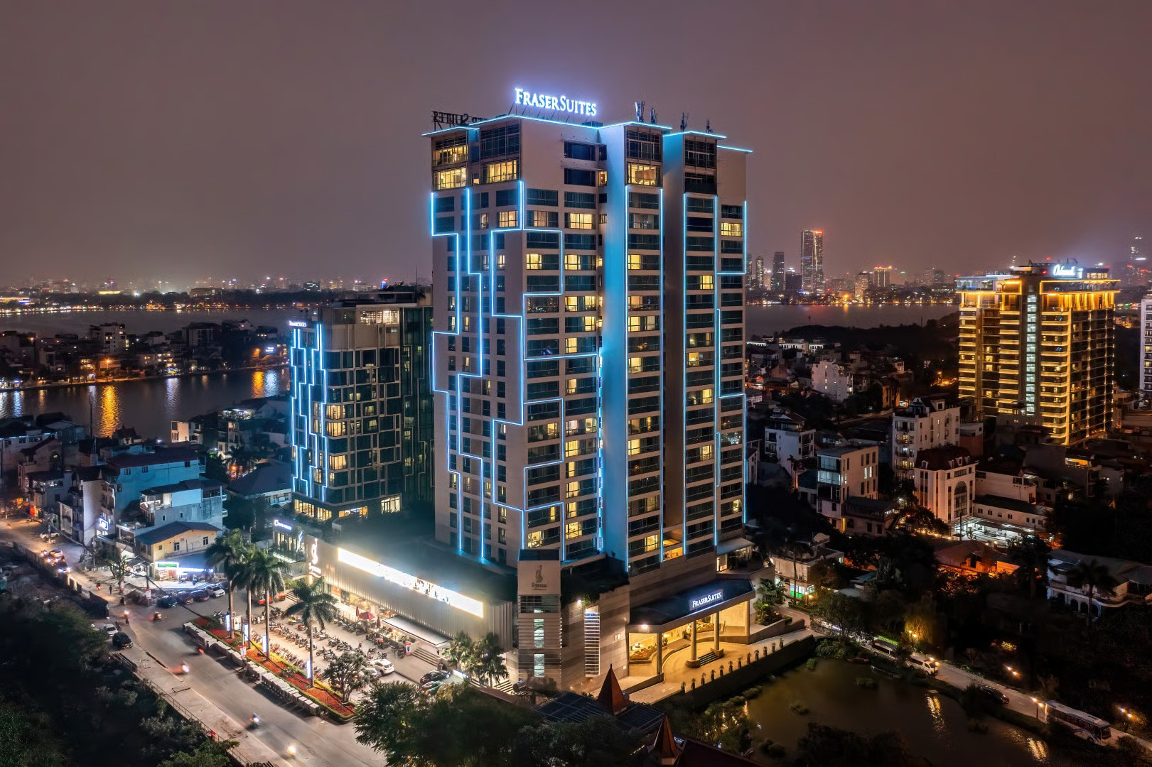 Fraser Suites Hanoi tower illuminated at night beside West Lake and the Hanoi skyline