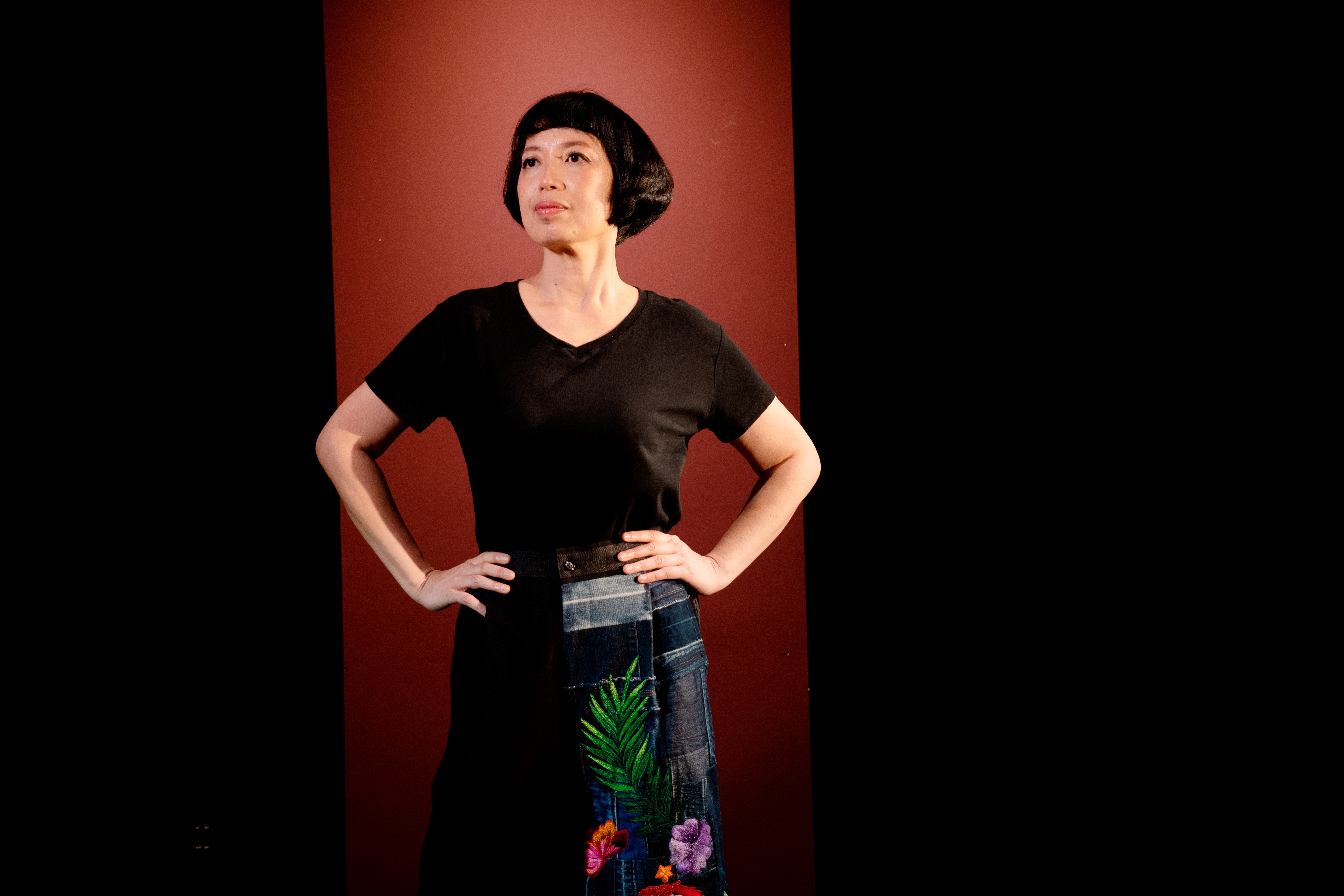 Tra Nguyen in a black top and embroidered denim skirt against a red backdrop