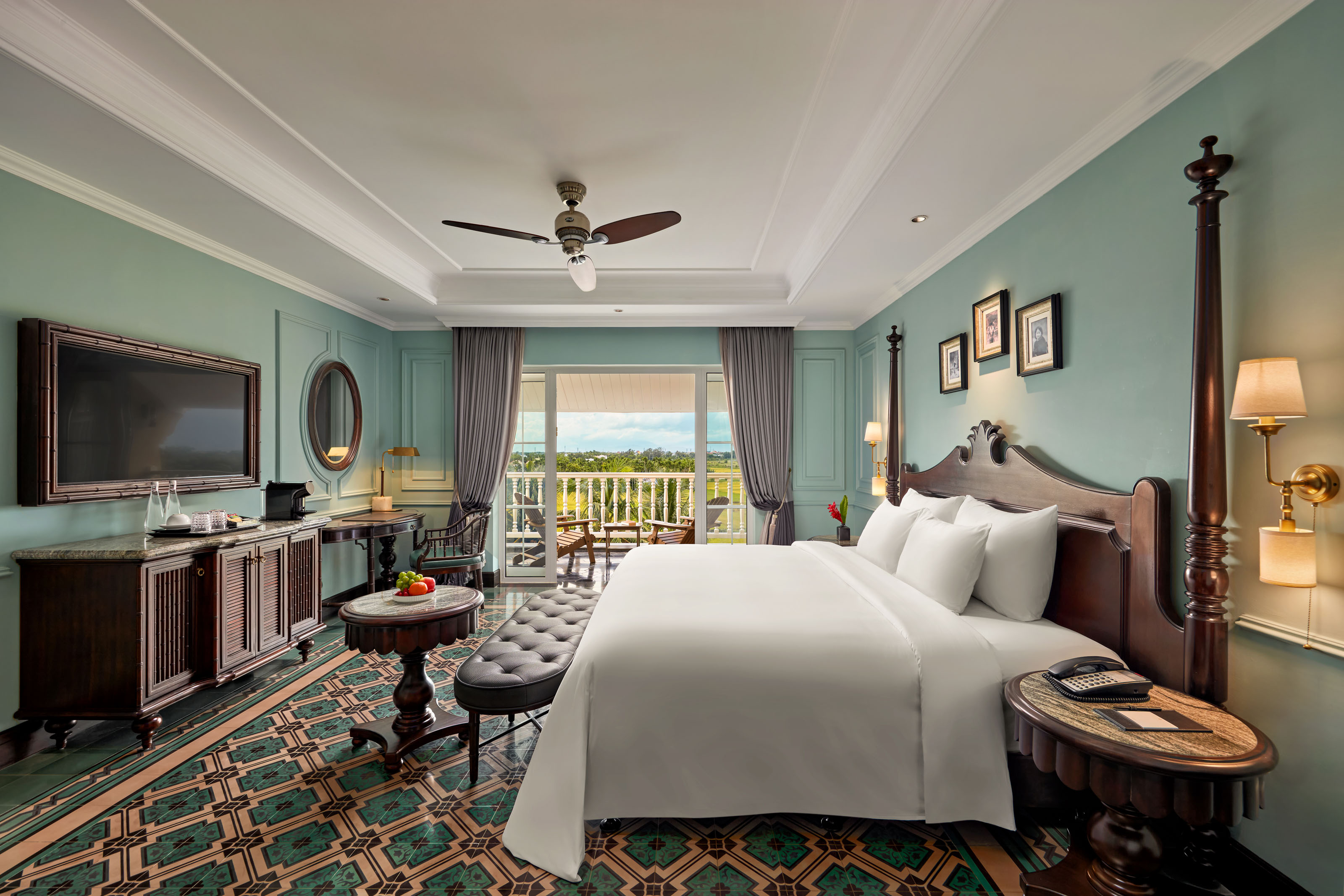 Executive suite at La Siesta Hoi An with mint-green walls, patterned tile floor, dark timber four-poster bed and a balcony overlooking rice fields.