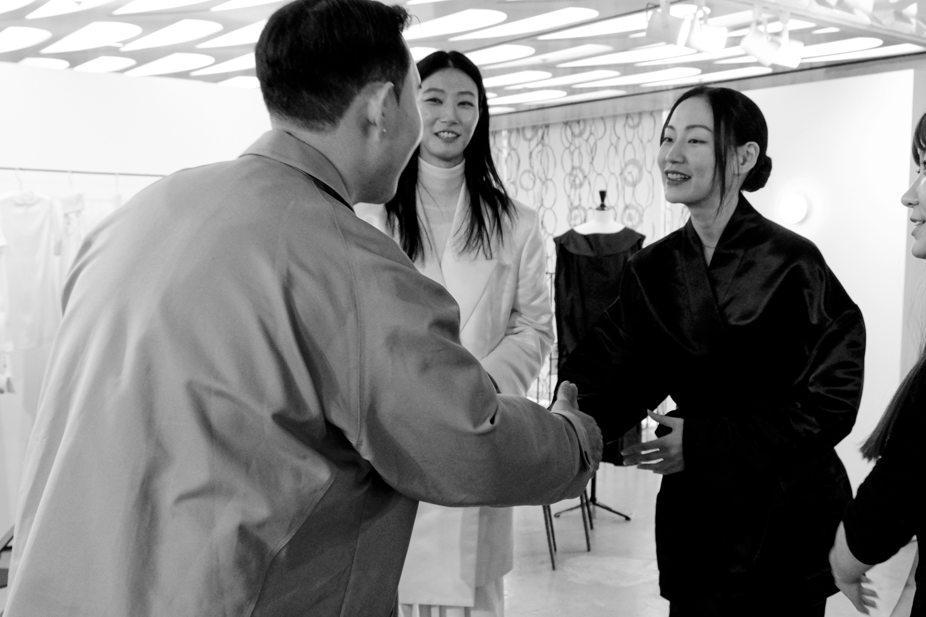 Black-and-white photo of guests greeting one another at the Gia Studios showroom, with garments on dress forms behind