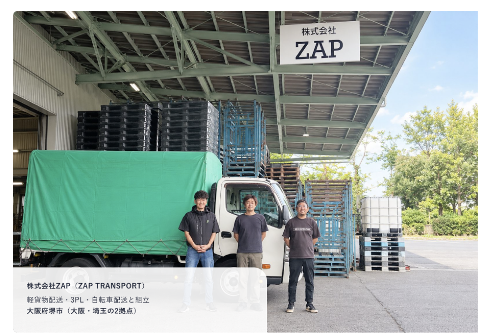 Three men in dark T-shirts stand beside a small truck with a green cover under a warehouse canopy signed ZAP.