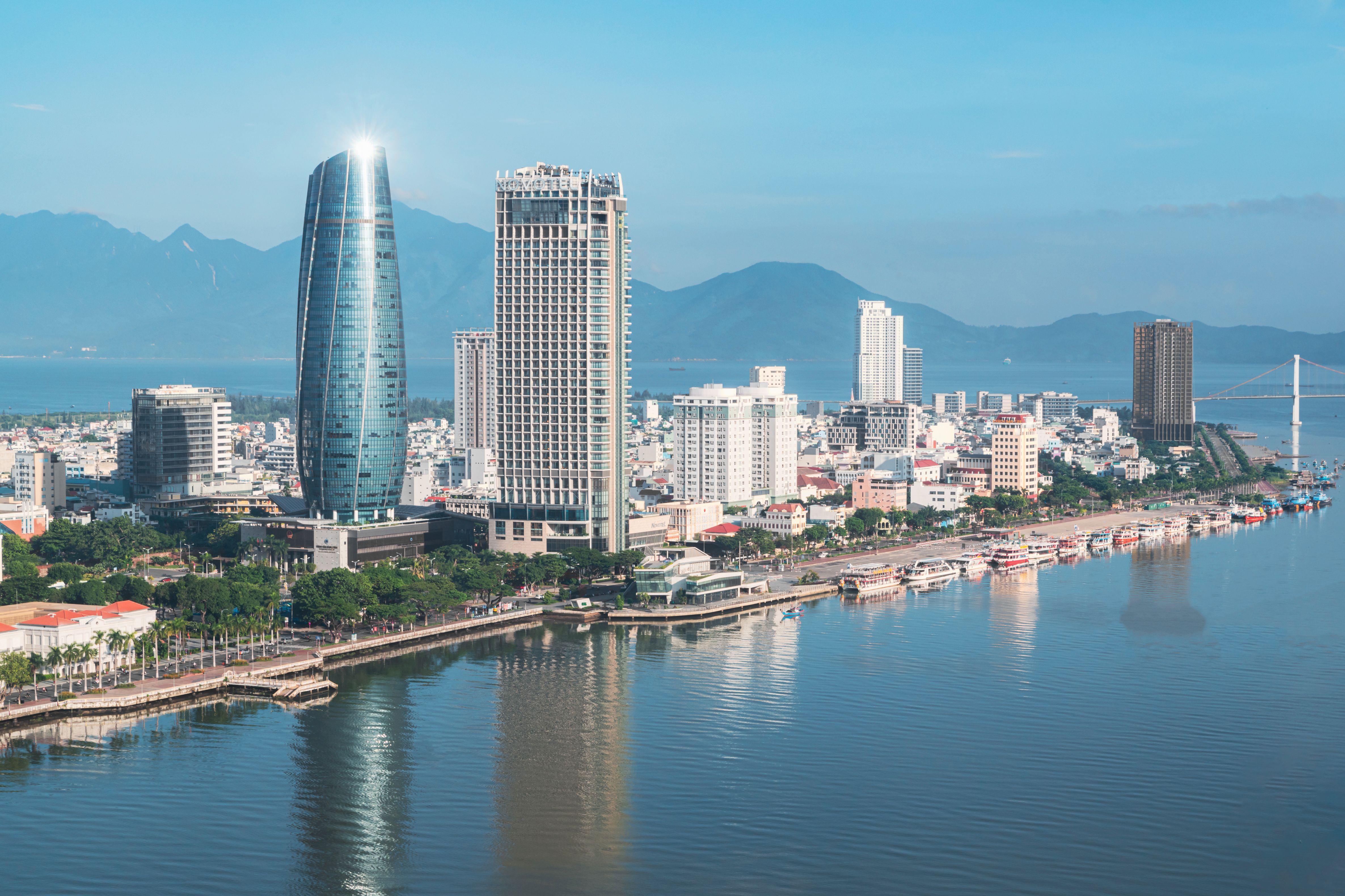 Da Nang's riverfront skyline along the Han River, with high-rise hotels and office towers against a mountain backdrop.